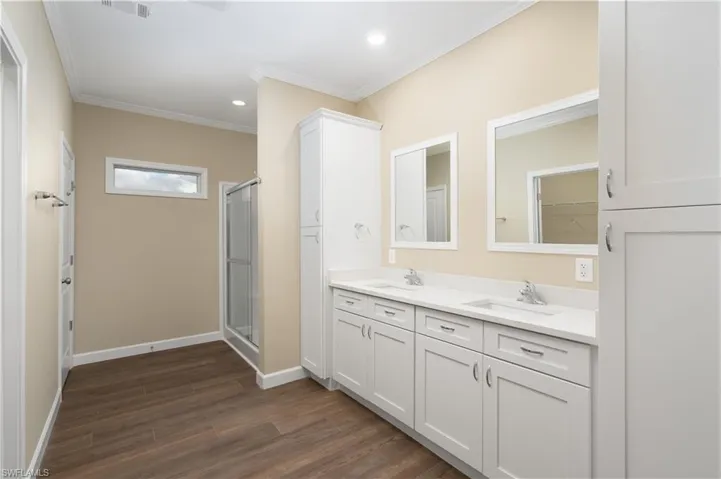 Bathroom with double vanity, dark wood-style floors, a stall shower, crown molding, and recessed lighting