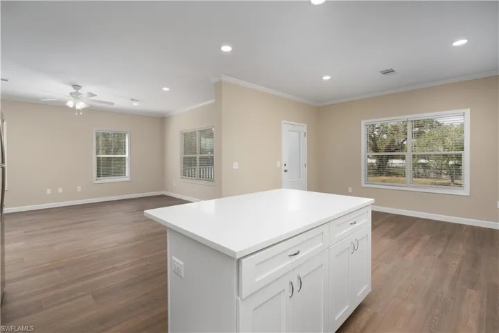 Kitchen with dark wood-style flooring, open floor plan, crown molding, ceiling fan, and a kitchen island