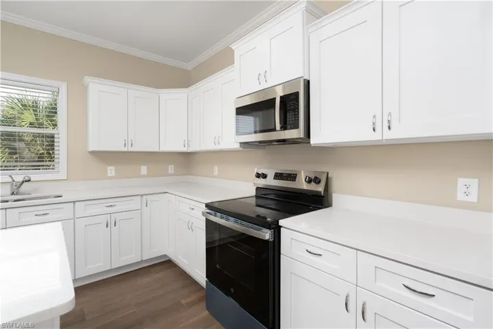 Kitchen with stainless steel appliances, white cabinetry, crown molding, and dark wood-style floors