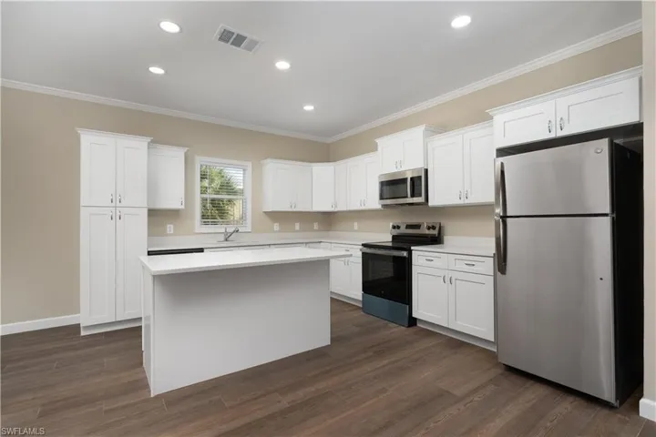 Kitchen with stainless steel appliances, white cabinets, a kitchen island, dark wood finished floors, and ornamental molding