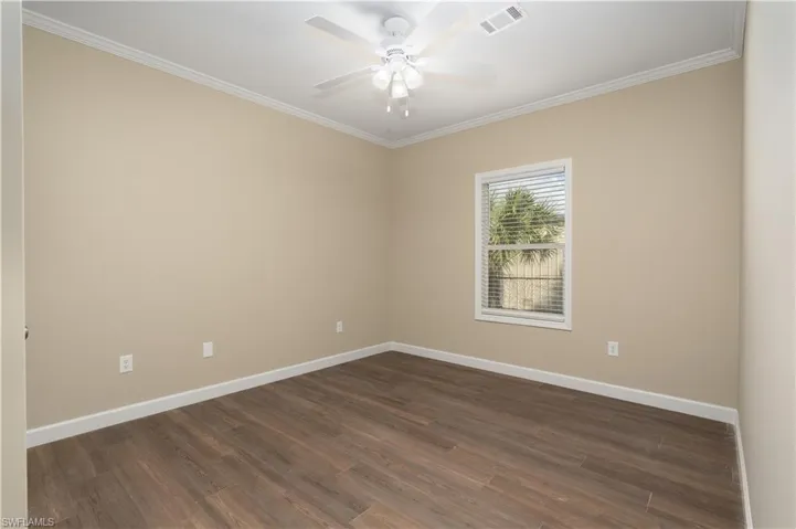 Empty room featuring crown molding, dark wood finished floors, and ceiling fan