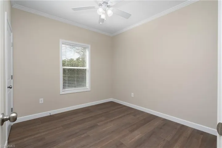 Empty room featuring ornamental molding, dark wood-style floors, and ceiling fan