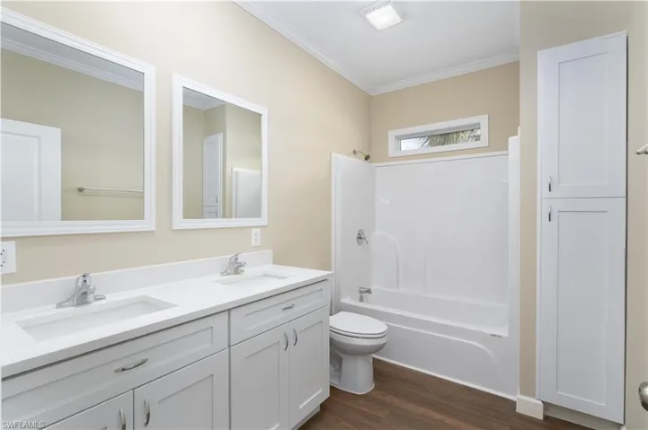 Full bathroom with double vanity, crown molding, dark wood-type flooring, and shower / tub combination