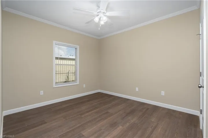 Empty room with dark wood finished floors, ornamental molding, and a ceiling fan