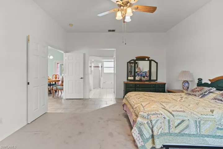 Carpeted bedroom featuring a ceiling fan with integrated lighting, white paneled doors, and an open doorway revealing a tiled area