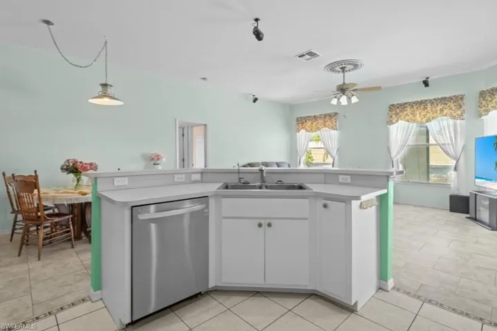Kitchen island featuring a double basin sink, stainless steel dishwasher, and white cabinetry