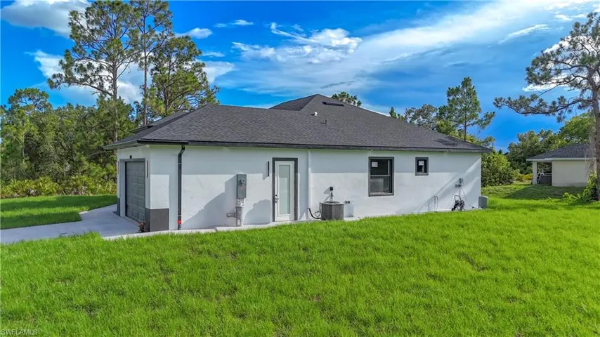 Rear view of property featuring stucco siding, a lawn, and a shingled roof