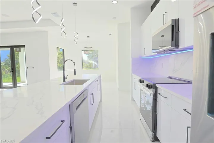 Kitchen with stainless steel appliances, decorative light fixtures, light tile patterned floors, white cabinets, and backsplash