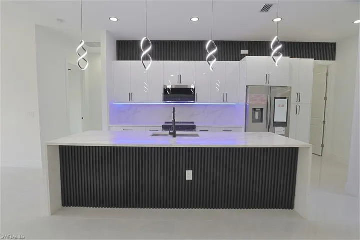 Kitchen with stainless steel appliances, a spacious island, white cabinetry, pendant lighting, and light tile patterned floors