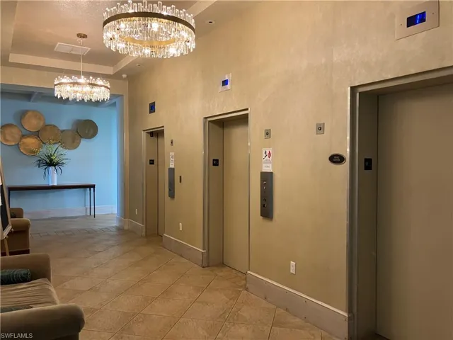 Lobby area featuring two crystal chandeliers, three elevators, tile flooring, and a decorative wall treatment