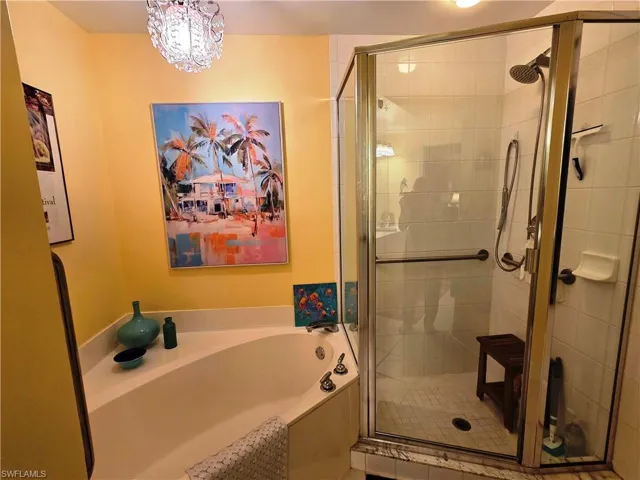 Bathroom featuring a corner soaking tub with deck-mounted fixtures, an enclosed glass shower with white tile surround, and a crystal chandelier