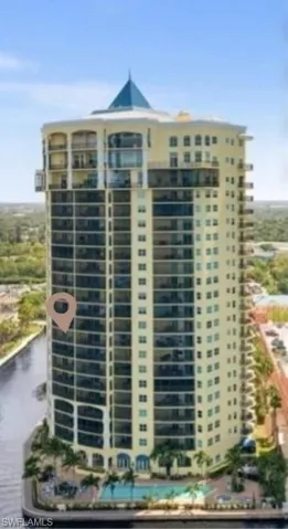 Multistory residential building with a conical rooftop, featuring numerous private balconies, a ground-level swimming pool, and direct waterfront access