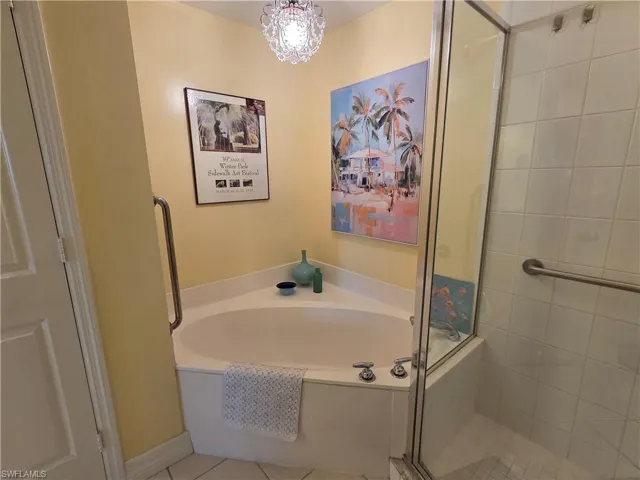 Bathroom featuring a corner soaking tub with deck-mounted fixtures, a glass-enclosed shower with white tiled walls, a crystal chandelier, and grab bars