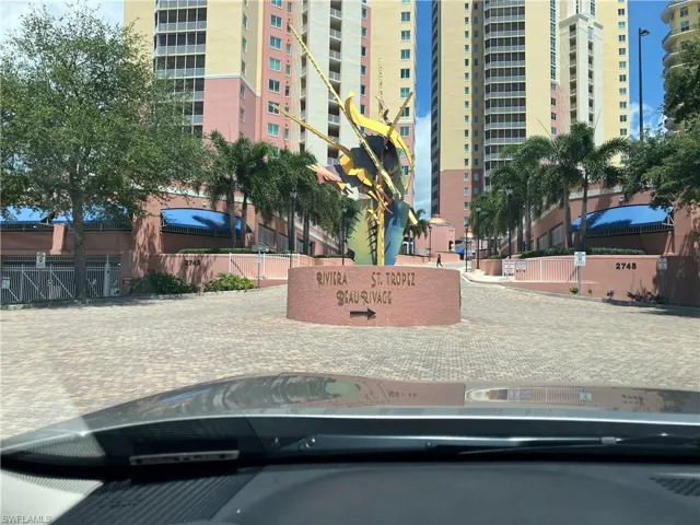 Paver driveway entrance featuring mature palm trees and a vibrant multi-story building facade