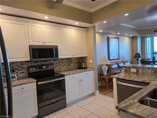 Contemporary kitchen featuring white cabinetry, a mosaic tile backsplash, stainless steel appliances, recessed lighting, and a breakfast bar with stone countertops