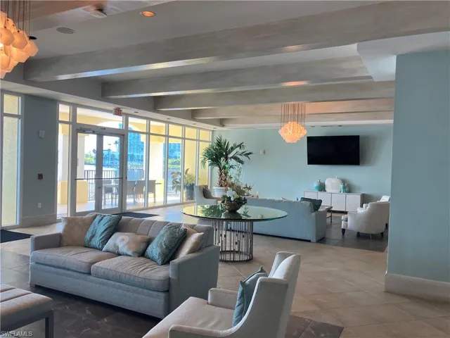 Spacious lounge area featuring a full wall of glass panels and doors, exposed ceiling beams, recessed lighting, and a large wall-mounted display
