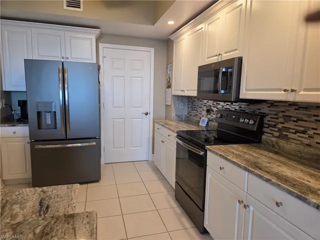 Kitchen featuring white shaker-style cabinetry, granite-finish countertops, and a full tile backsplash
