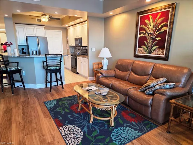 Open-concept living space featuring wood-finish flooring, a kitchen with white cabinetry, stainless steel refrigerator, and a breakfast bar with seating