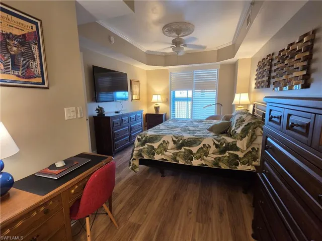 Spacious room featuring wood-finish flooring, a tray ceiling with a decorative ceiling fan, and large windows with horizontal blinds