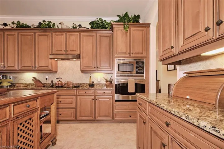 Kitchen featuring light stone countertops, backsplash, stainless steel appliances, and crown molding