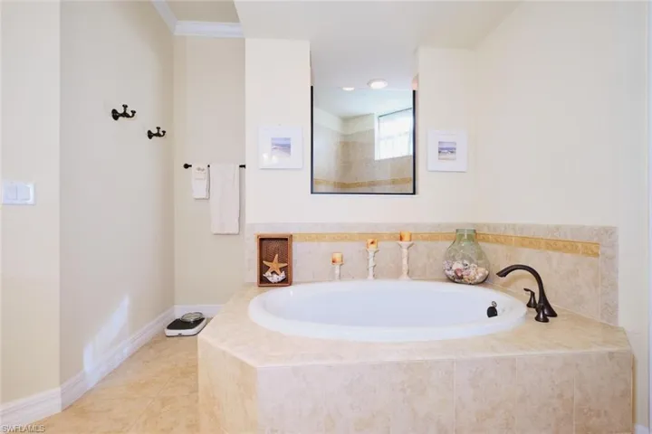 Bathroom with tile patterned flooring, crown molding, and tiled bath