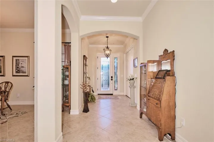 Tiled entryway featuring french doors, ornamental molding, and a notable chandelier