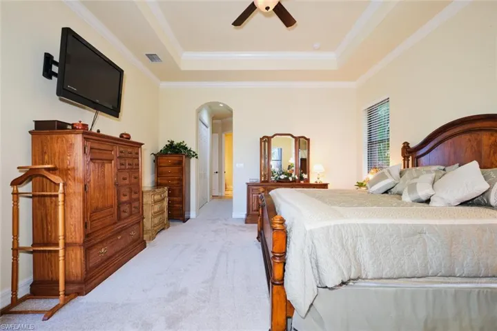 Bedroom with a raised ceiling, ceiling fan, light carpet, and ornamental molding