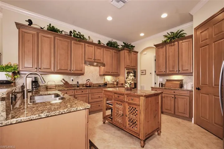 Kitchen featuring a center island, crown molding, sink, tasteful backsplash, and light stone counters