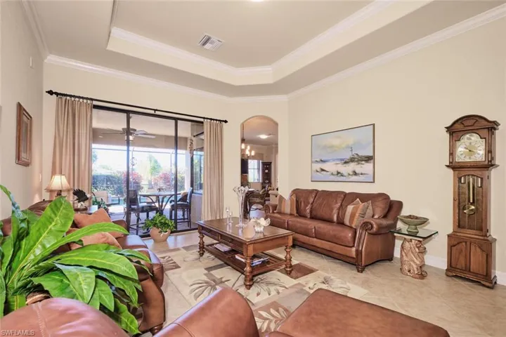 Living room featuring ceiling fan with notable chandelier, light tile patterned flooring, coffered ceiling, and ornamental molding