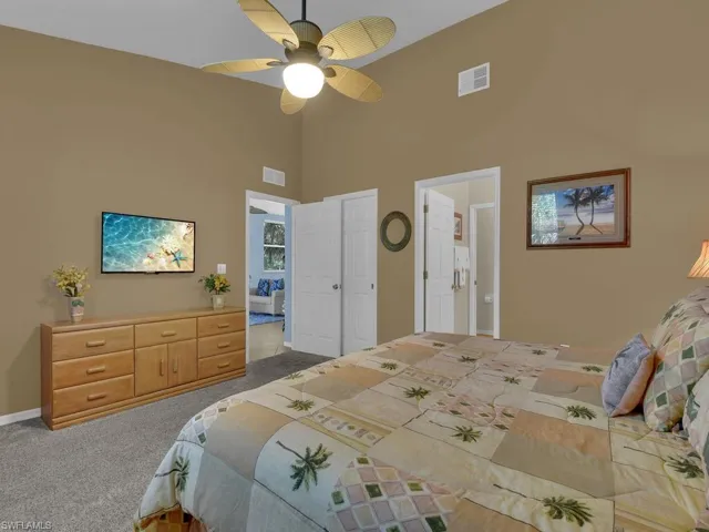 Vaulted ceiling bedroom featuring a ceiling fan with integrated lighting, two white panel doors, and neutral carpet flooring
