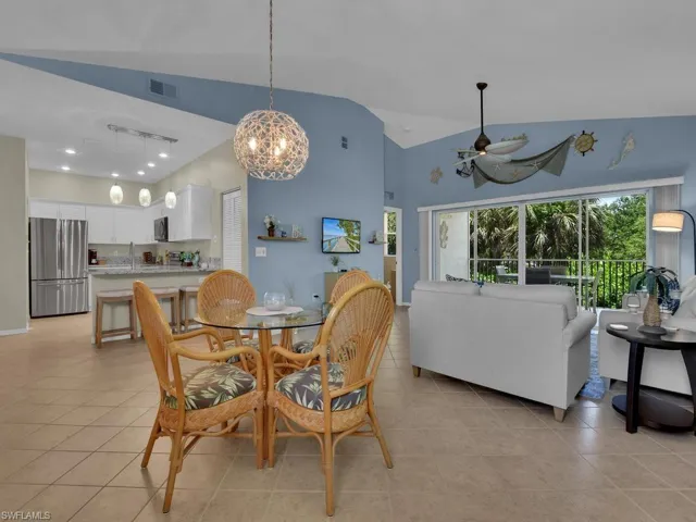 Open-concept living area with vaulted ceilings, neutral tile flooring, and a kitchen featuring white cabinetry, stainless steel appliances, and a breakfast bar