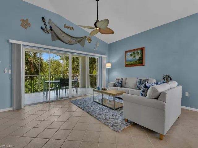Spacious living area featuring neutral tile flooring, vaulted ceilings, and a ceiling fan