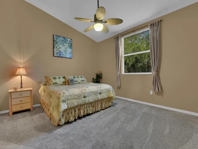 Vaulted ceiling with a ceiling fan, neutral wall paint, window with blinds and drapery, and gray carpet flooring