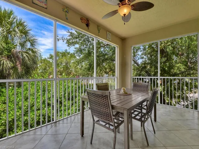 Screened lanai featuring tile flooring, a ceiling fan with integrated lighting, and white railings overlooking lush greenery