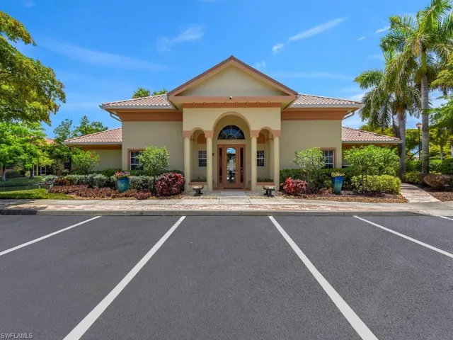 Mediterranean-style building with a terracotta tile roof, stucco exterior, arched entryway, extensive landscaping, and adjacent paved parking