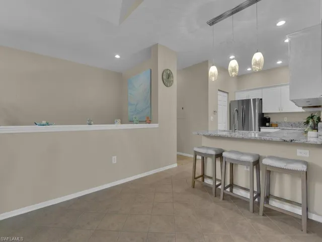 Open-concept kitchen with a breakfast bar, white cabinetry, granite countertops, stainless steel appliances, and tile flooring