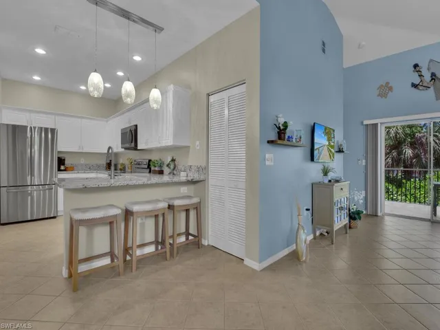 Open-concept kitchen featuring white cabinetry, stainless steel appliances, and a breakfast bar with granite-style countertops