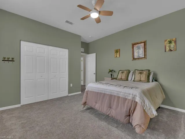 Spacious bedroom featuring neutral wall tones, gray carpeting, a ceiling fan with integrated lighting, and white bi-fold closet doors