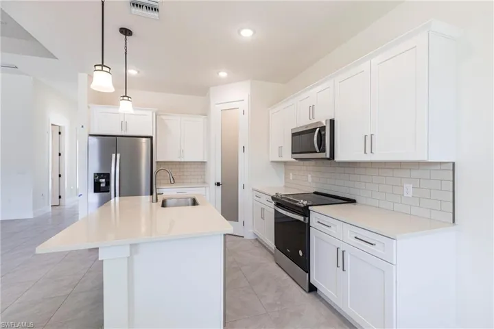 Kitchen with stainless steel appliances, a sink, white cabinets, light countertops, and decorative light fixtures