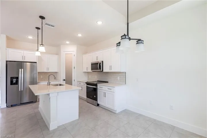 Kitchen with stainless steel appliances, light countertops, decorative light fixtures, and white cabinetry