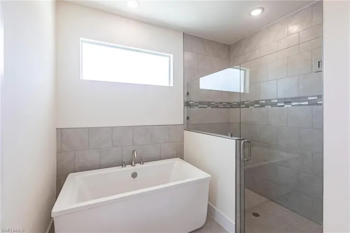 Bathroom featuring a shower stall, tile walls, a freestanding bath, and recessed lighting