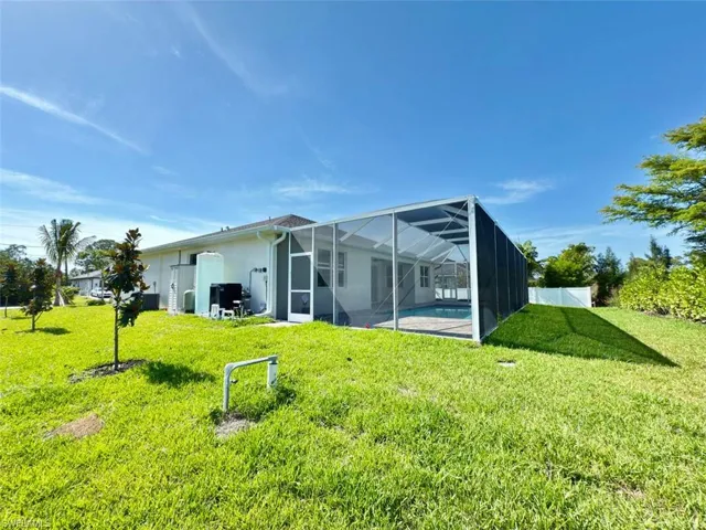 Rear view of house with a lawn, glass enclosure, an outdoor pool, and stucco siding
