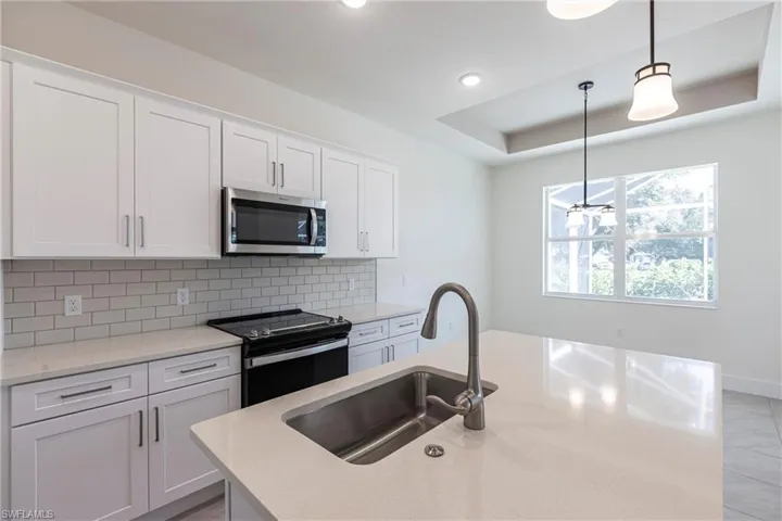 Kitchen with stainless steel microwave, electric range oven, a kitchen island with sink,