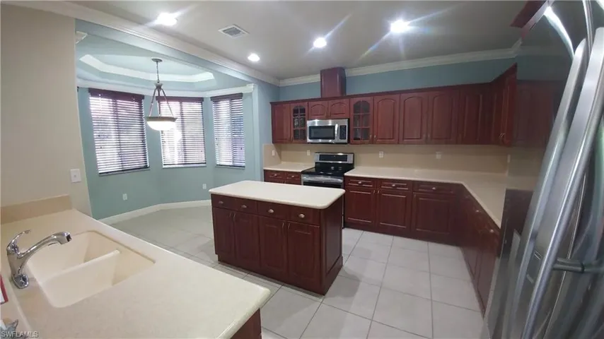 Kitchen with stainless steel appliances, glass fronted cabinets, light countertops, light tile patterned floors, and crown molding