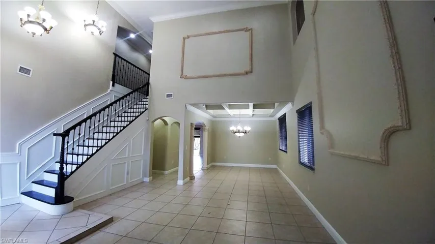 Entryway featuring suspended lighting, crown molding, light tile floors, arched walkways, and volume ceiling