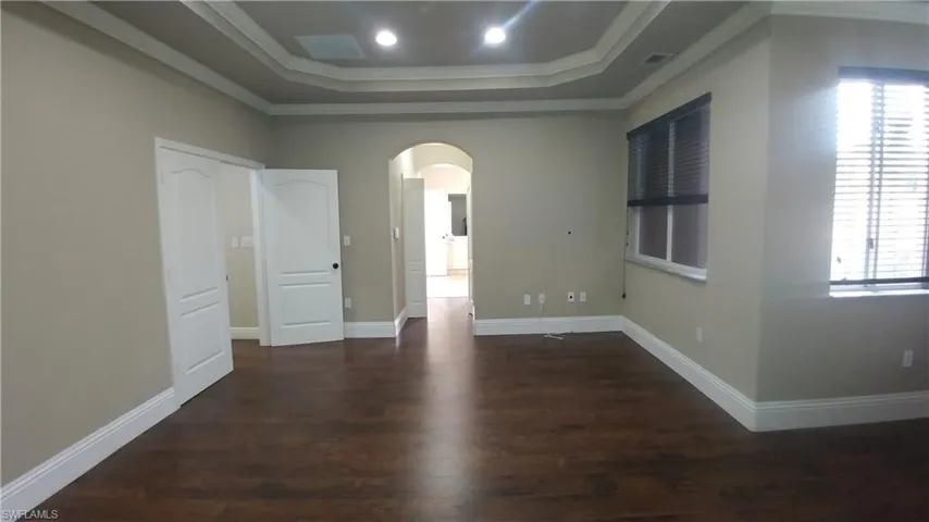 Empty room featuring arched walkways, dark wood finished floors, and ornamental molding