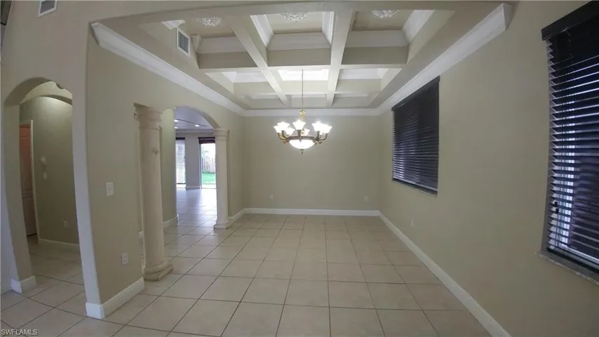 Suuspended Chandelier from coffered ceiling, crown molding, tile floors, and arched walkways