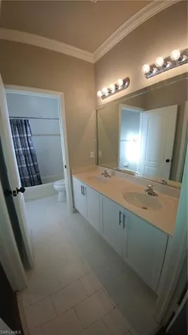 Bathroom with double vanity, crown molding, and shower / bathtub combination with curtain