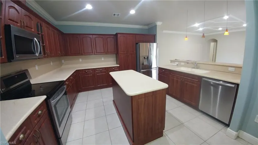 Kitchen with stainless steel appliances, light countertops, a kitchen island, pendant lighting, and ornamental molding