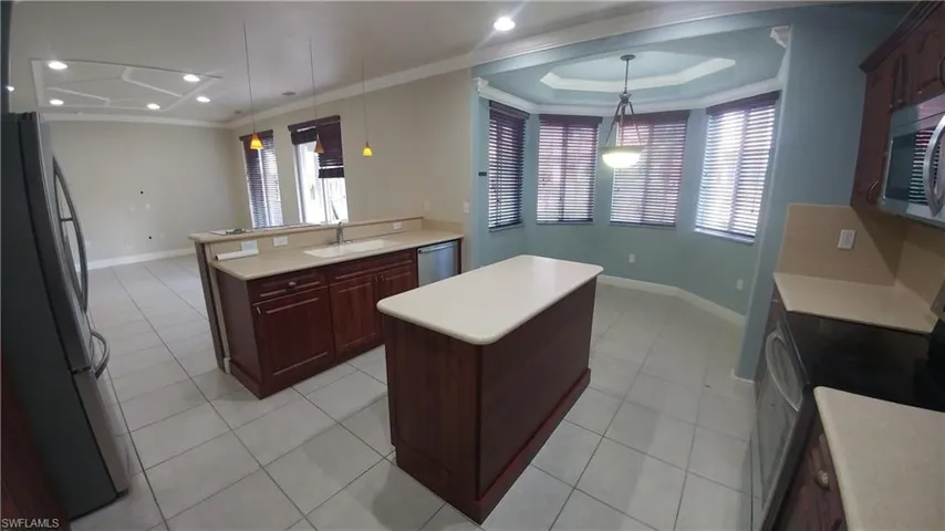 Kitchen with stainless steel appliances, crown molding, a kitchen island, pendant lighting, and light tile patterned floors